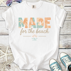 White t-shirt with 'MADE for the beach' graphic, featuring coastal colors and tropical designs.