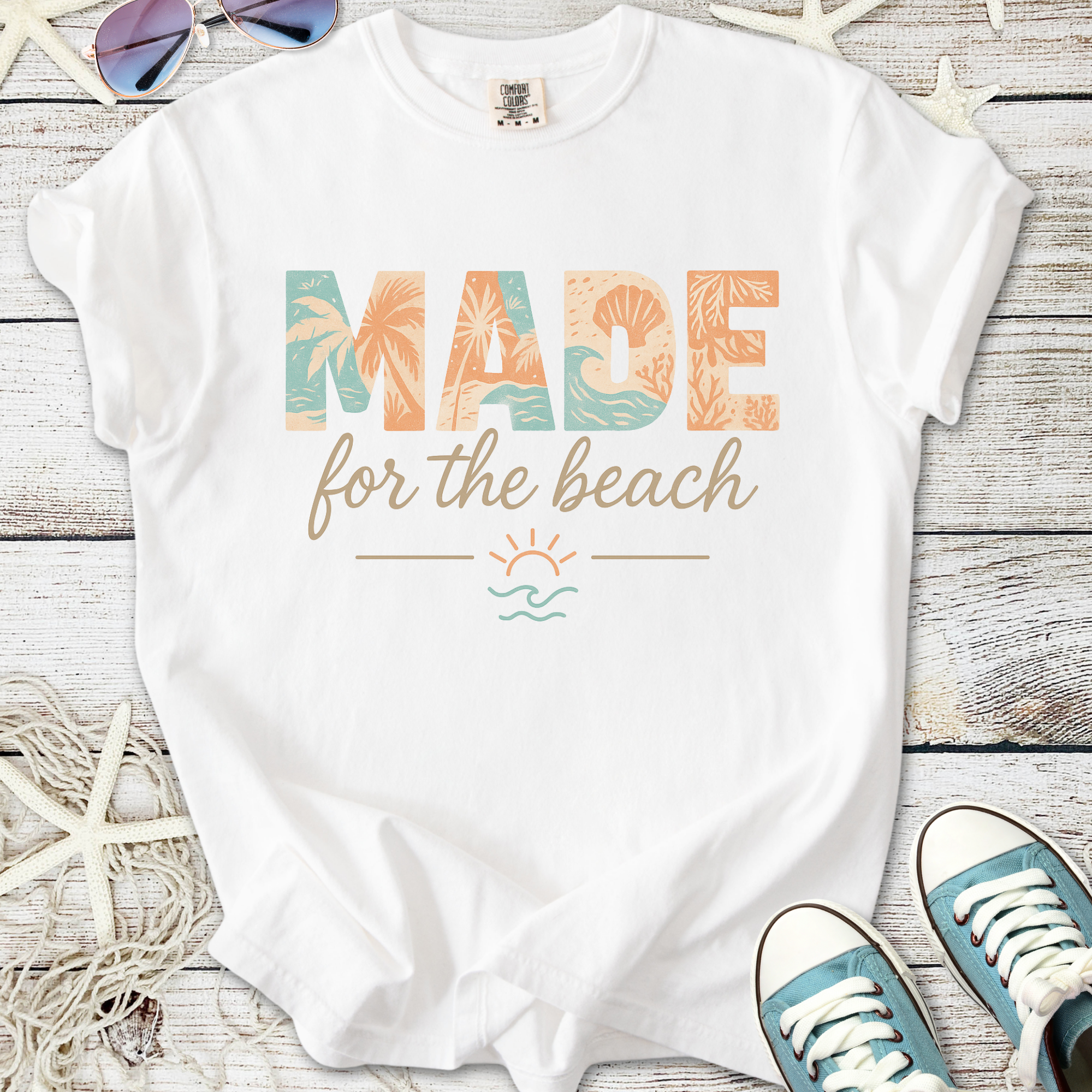 White t-shirt with 'MADE for the beach' graphic, featuring coastal colors and tropical designs.
