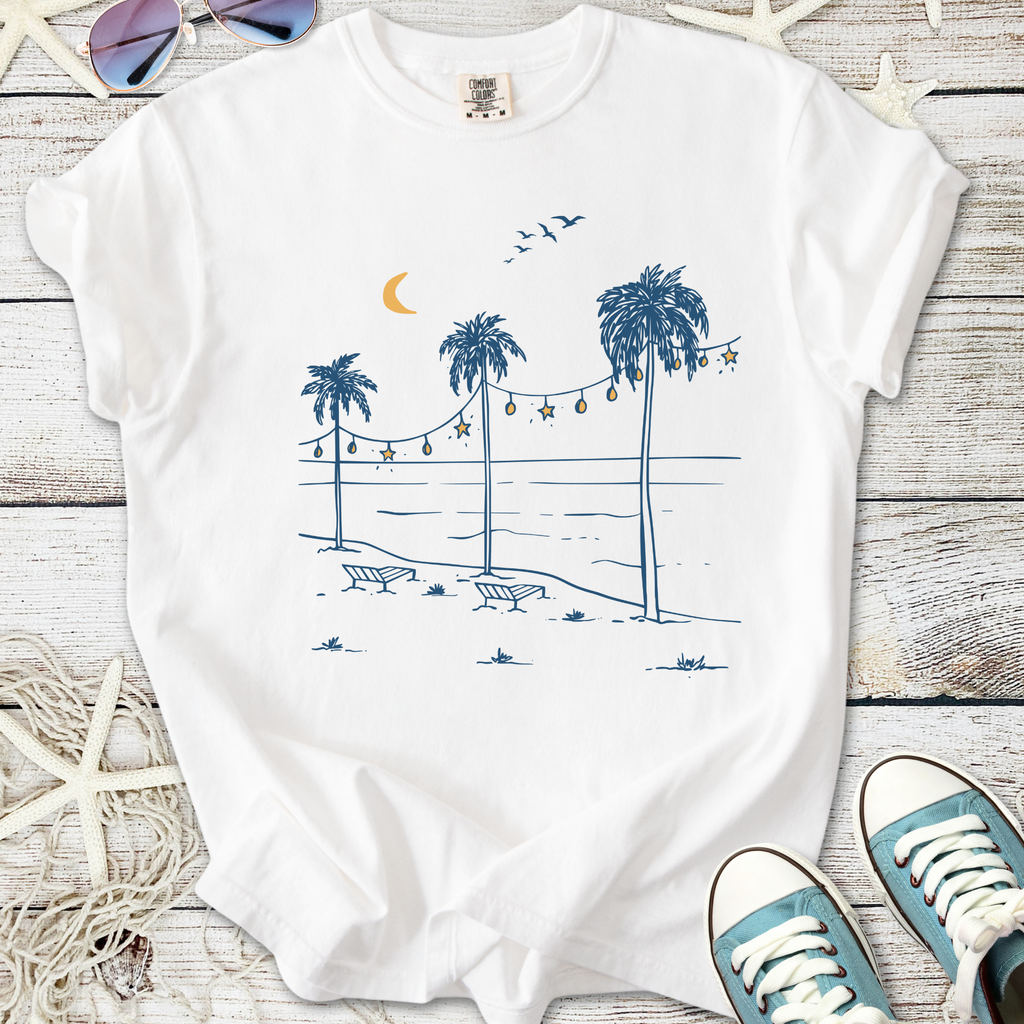 White t-shirt featuring a tropical beach scene with palm trees, sunset, and lounge chairs in blue ink.