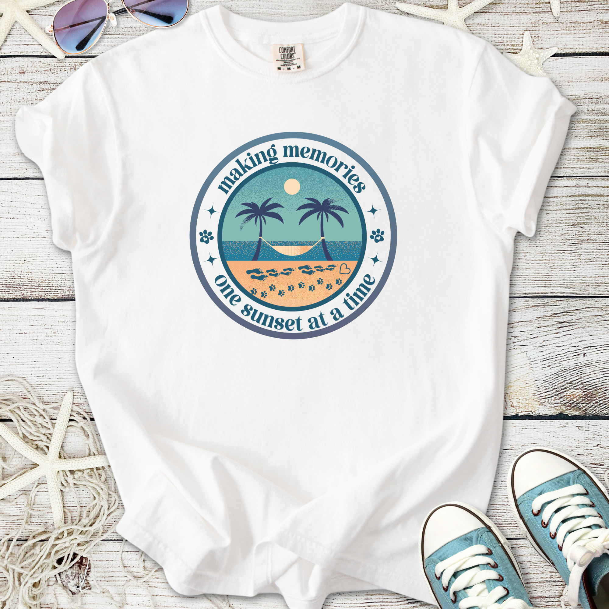 White t-shirt with sunset graphic design, featuring palm trees and beach, perfect for summer memories.
