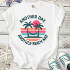 White graphic t-shirt with 'Another Day, Another Beach Nap' and palm tree design, perfect for summer.