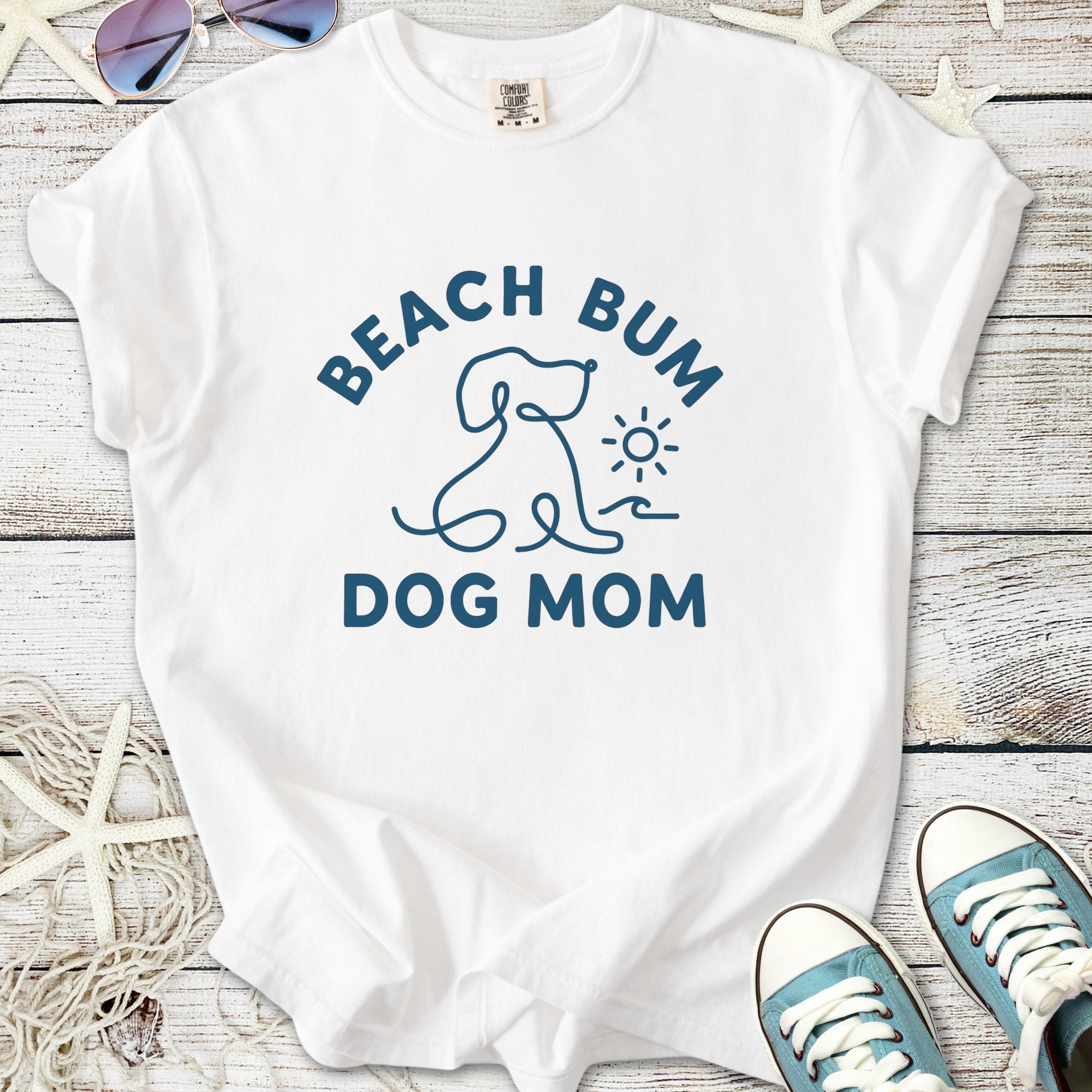 White t-shirt featuring 'Beach Bum Dog Mom' design with a dog and sun graphic, perfect for dog lovers.