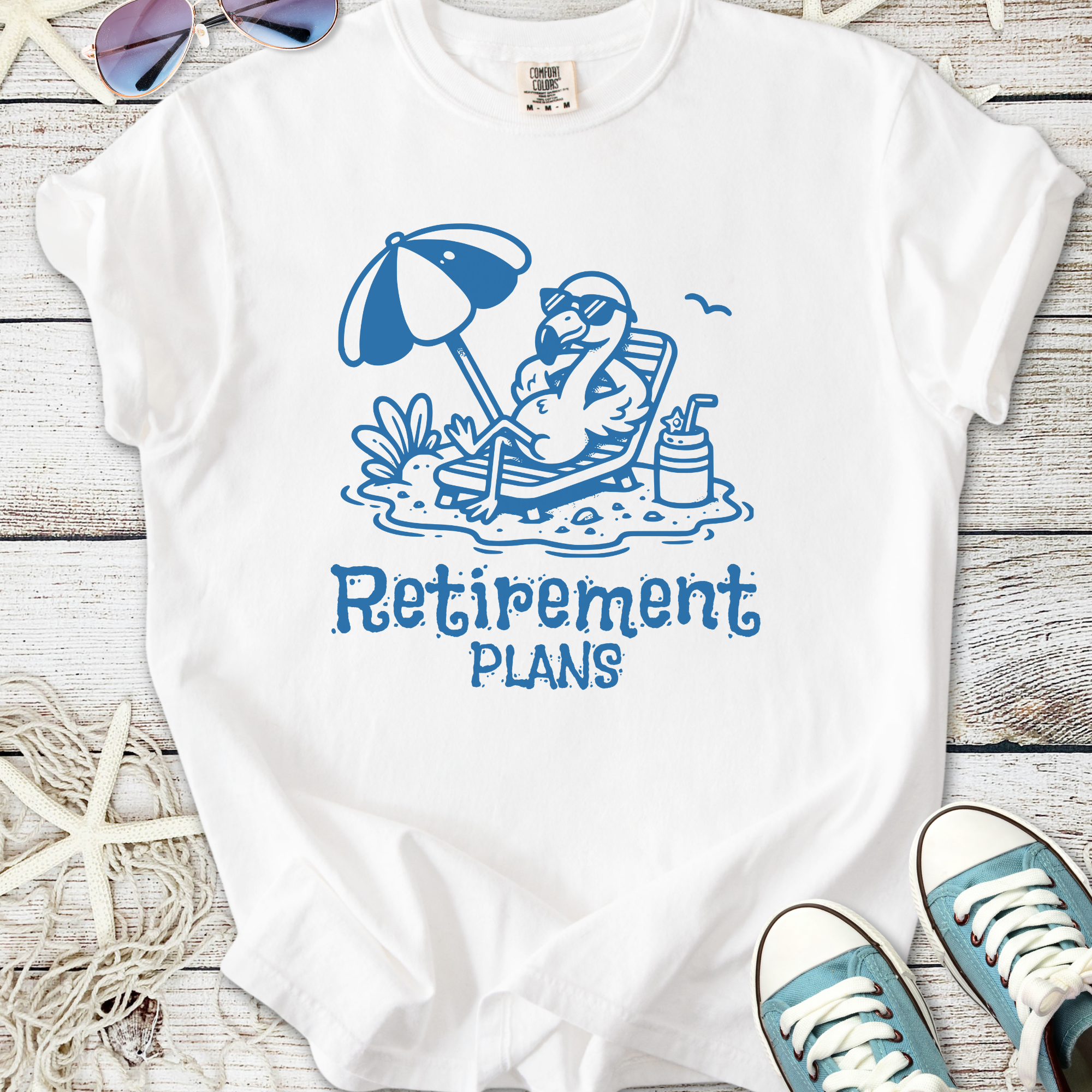 White t-shirt with a blue flamingo graphic and 'Retirement Plans' slogan, perfect for casual wear.
