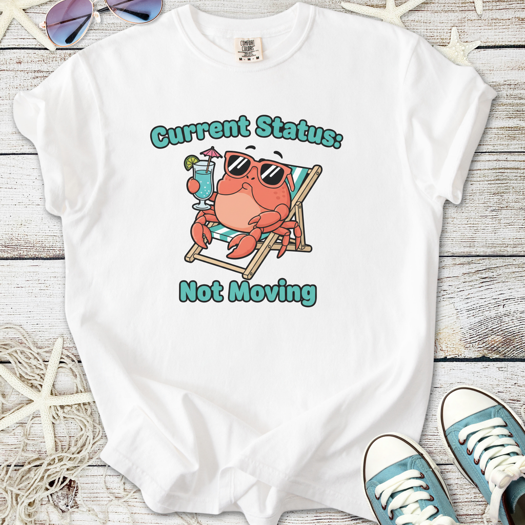 White t-shirt featuring a cute crab graphic with sunglasses and a drink, captioned 'Current Status: Not Moving'.