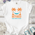 White t-shirt featuring a vibrant design with palm trees, hammock, and 'Retired: Sun, Sand & Sleep' text.