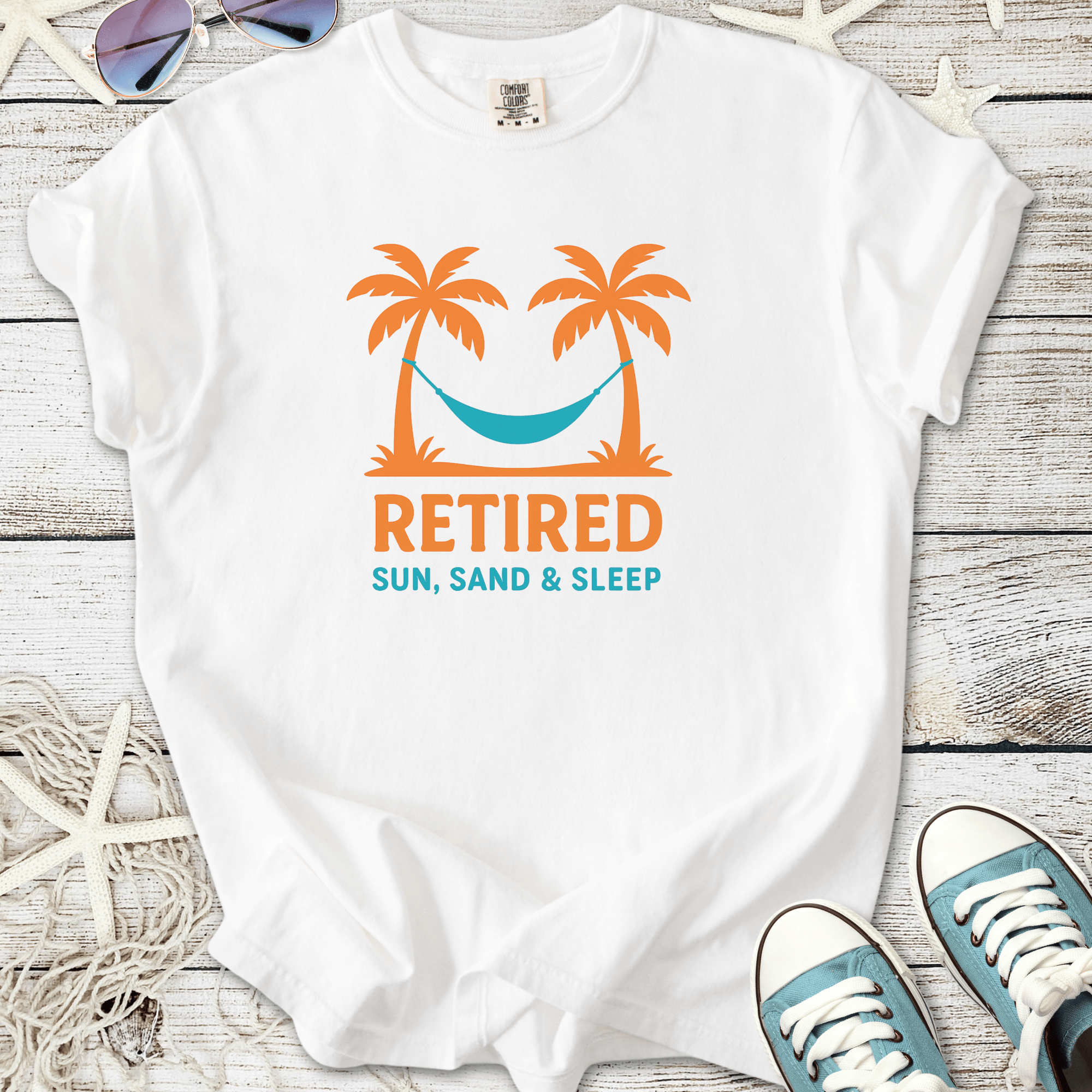 White t-shirt featuring a vibrant design with palm trees, hammock, and 'Retired: Sun, Sand & Sleep' text.