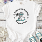White t-shirt featuring a cute dog graphic, text "My therapist has four paws & a beach pass", perfect for dog lovers.