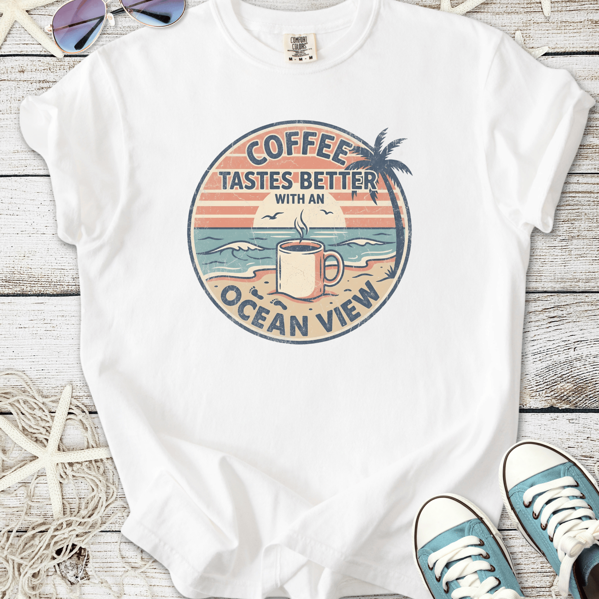 White graphic t-shirt featuring 'Coffee Tastes Better with an Ocean View' design, summer vibes.