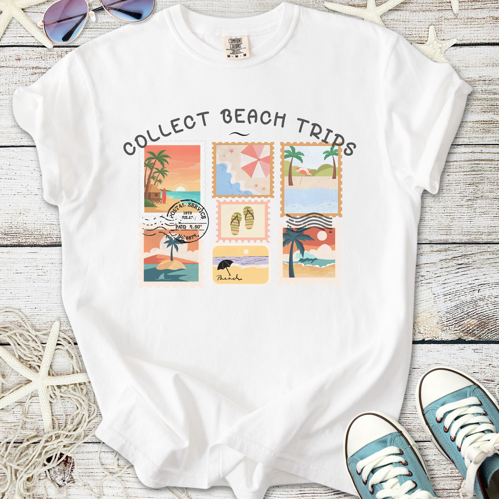 White t-shirt with 'Collect Beach Trips' graphic featuring colorful beach-themed stamps and illustrations.