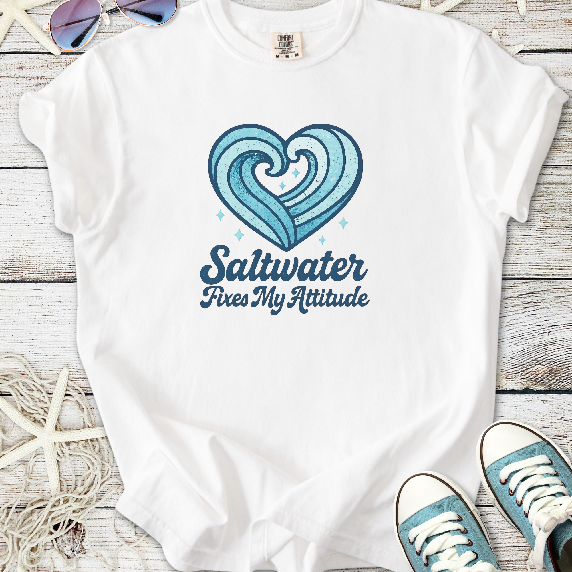 White t-shirt with heart wave graphic and 'Saltwater Fixes My Attitude' slogan, perfect for beach lovers.