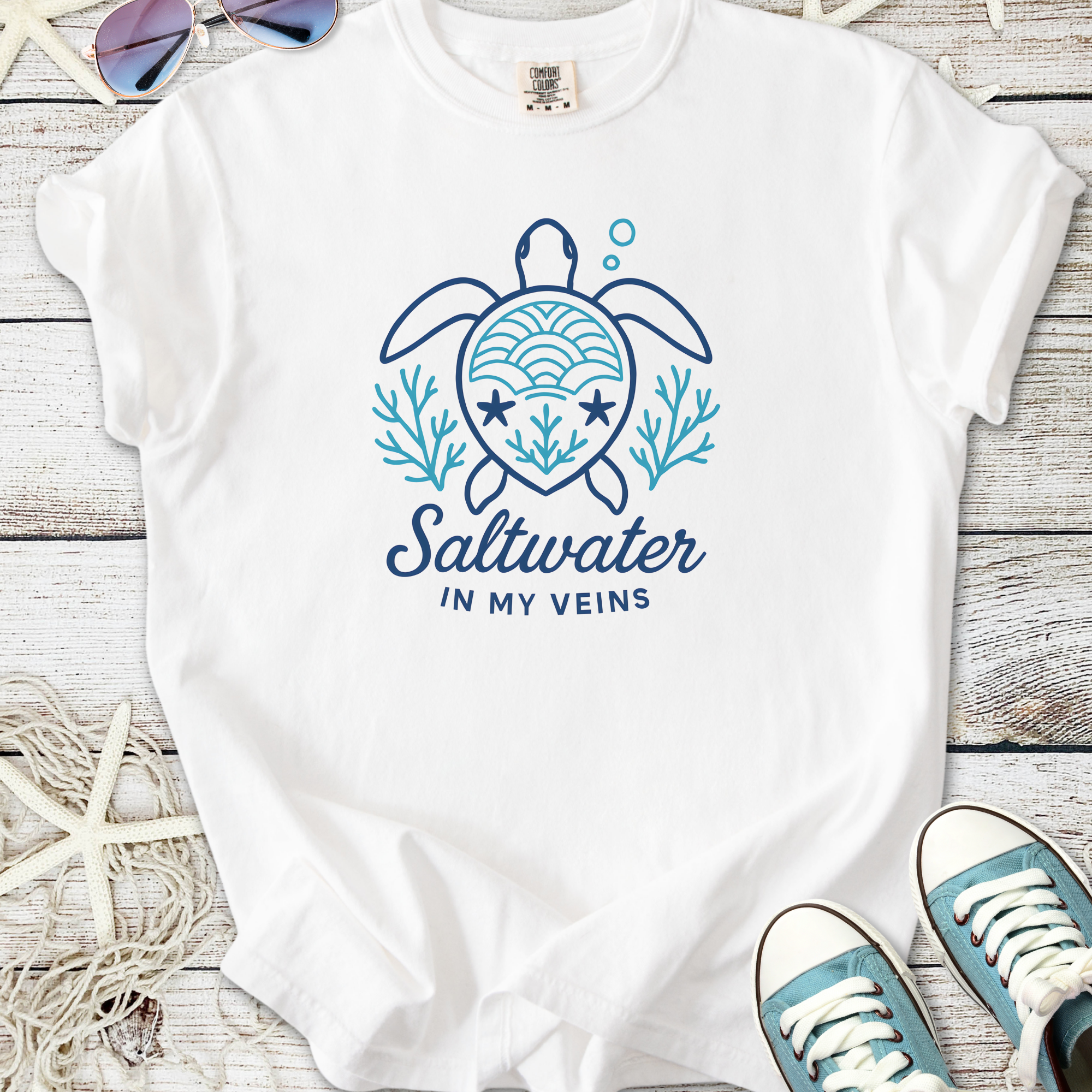 White t-shirt featuring a turtle graphic and 'Saltwater in my veins' text, perfect for beach lovers.