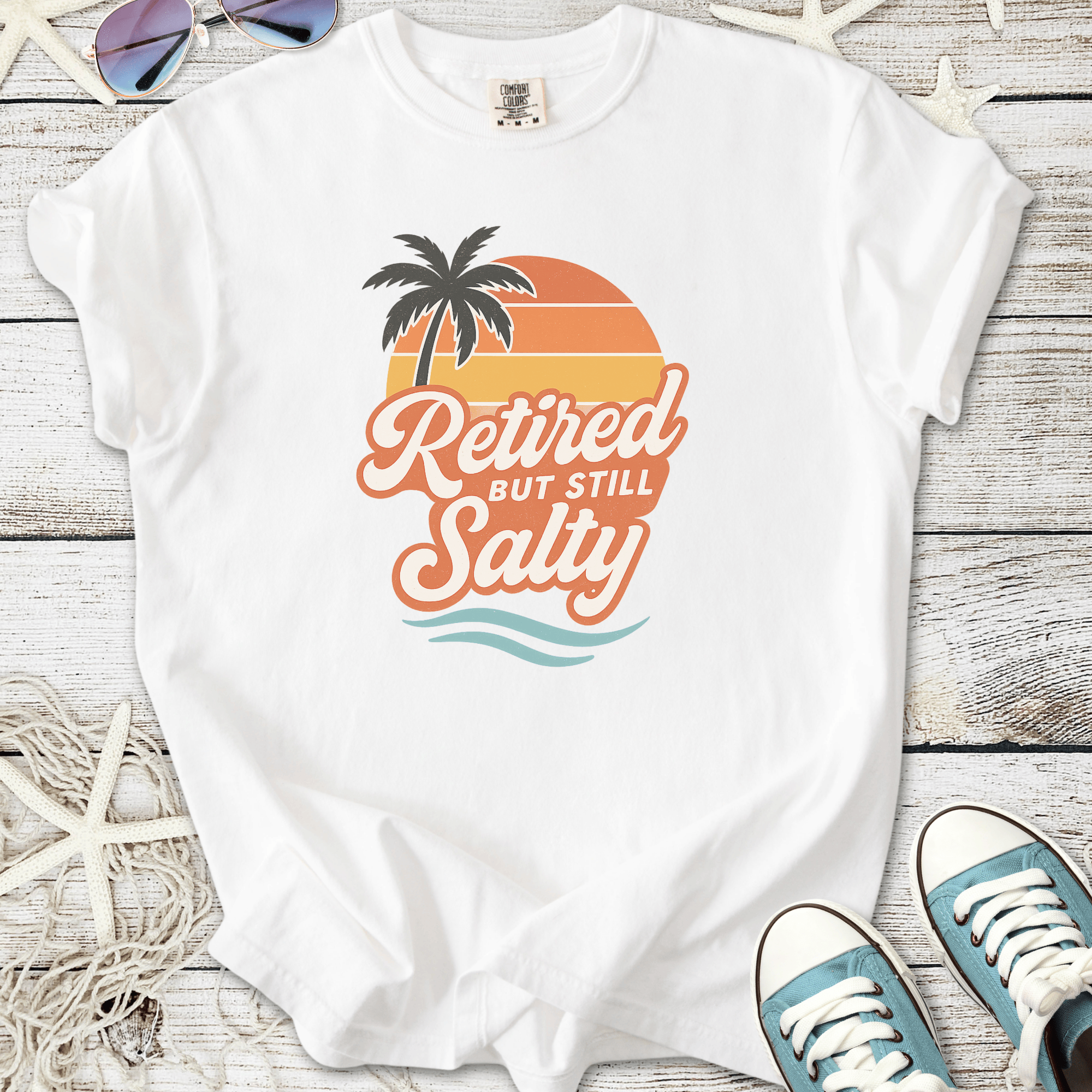 White t-shirt featuring 'Retired but Still Salty' graphic with palm tree and sunset design.