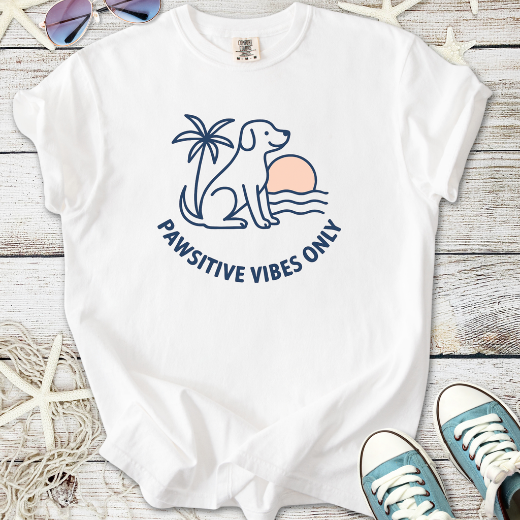 White t-shirt featuring dog, palm tree, and sunset design with 'Pawsitive Vibes Only' slogan.