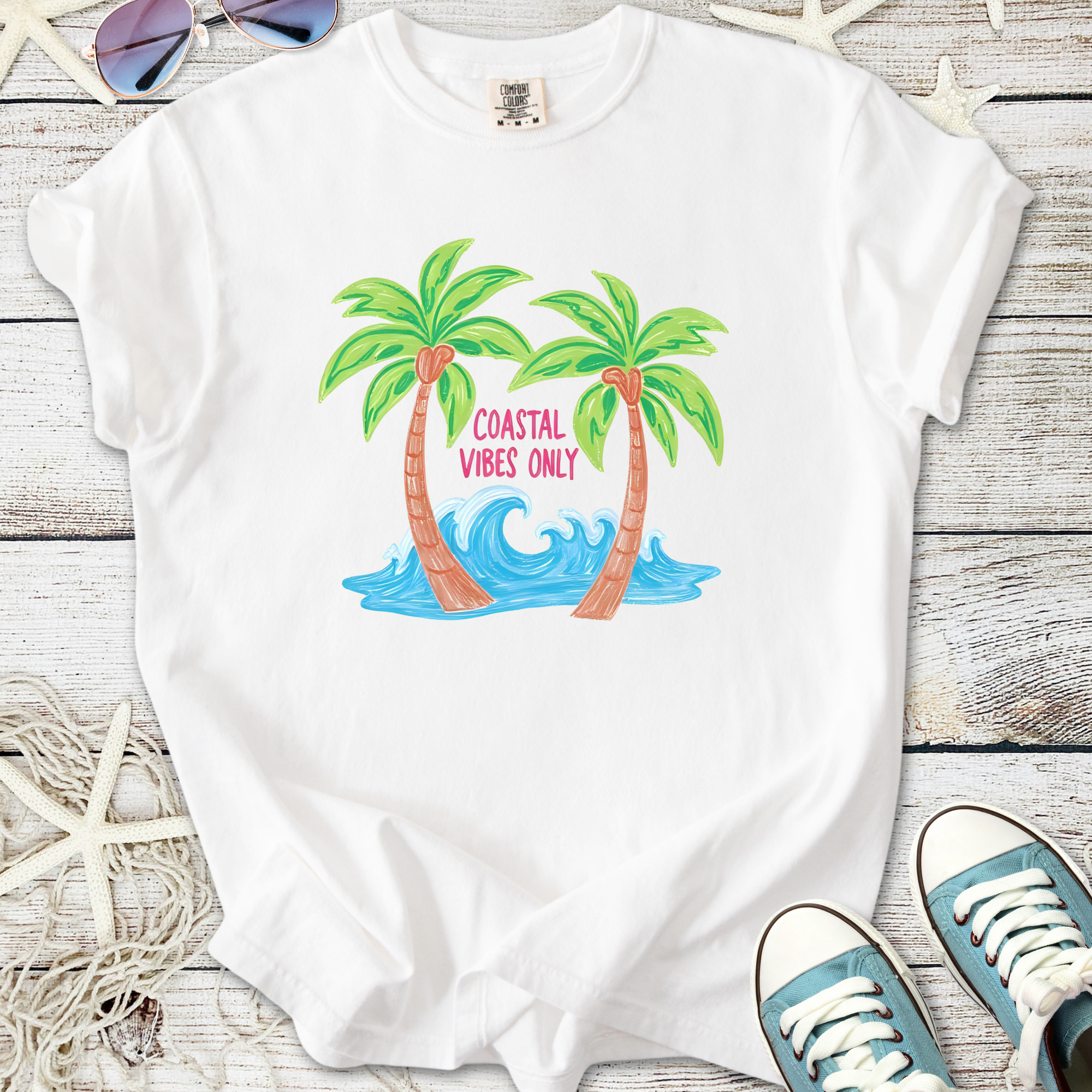 White t-shirt featuring palm trees and wave design with 'Coastal Vibes Only' text, perfect for summer.