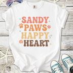 White t-shirt with colorful 'Sandy Paws Happy Heart' graphic, perfect for casual beach outings.
