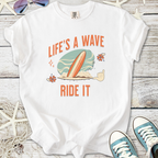 White graphic t-shirt with 'Life's a Wave Ride It' text and surfboard design, perfect for beach lovers.