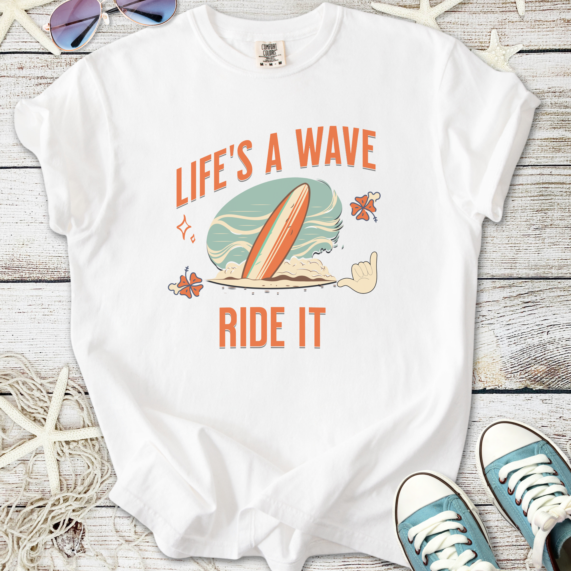 White graphic t-shirt with 'Life's a Wave Ride It' text and surfboard design, perfect for beach lovers.