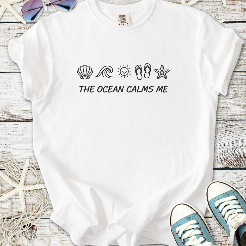 White t-shirt with 'THE OCEAN CALMS ME' and ocean-themed icons, perfect for beach lovers.