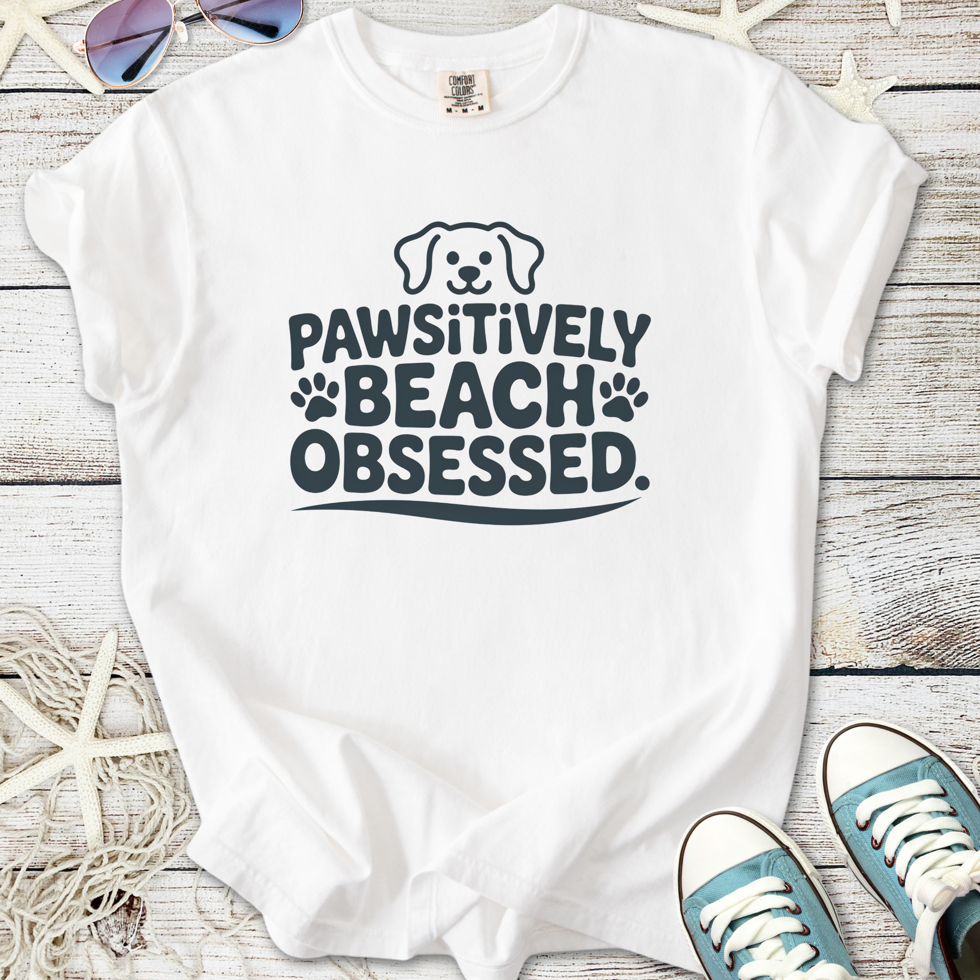 White t-shirt with 'Pawsitively Beach Obsessed' print, featuring a cute dog graphic and beach-themed design.