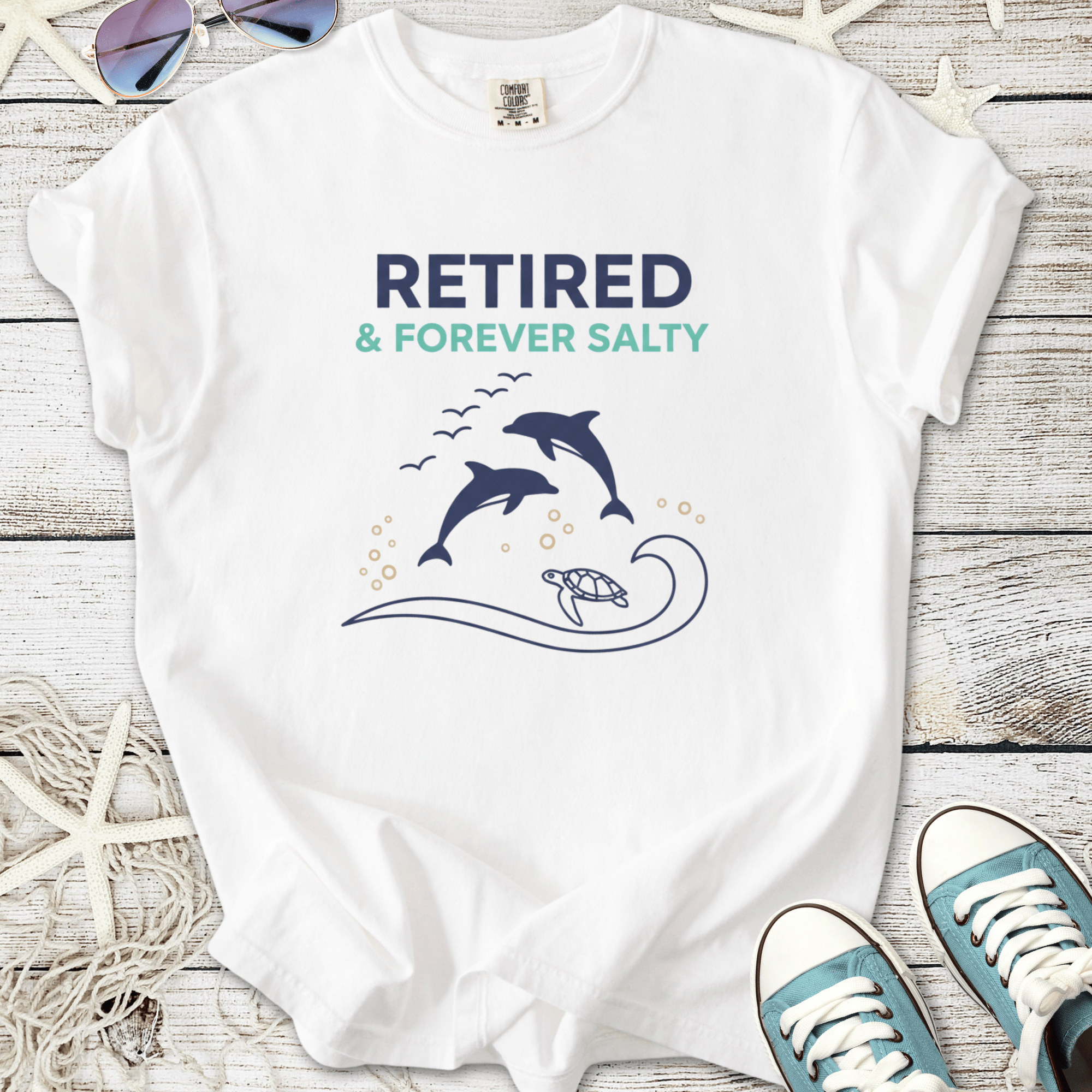 White t-shirt featuring dolphin and turtle graphic, text 'Retired & Forever Salty', casual beach style.