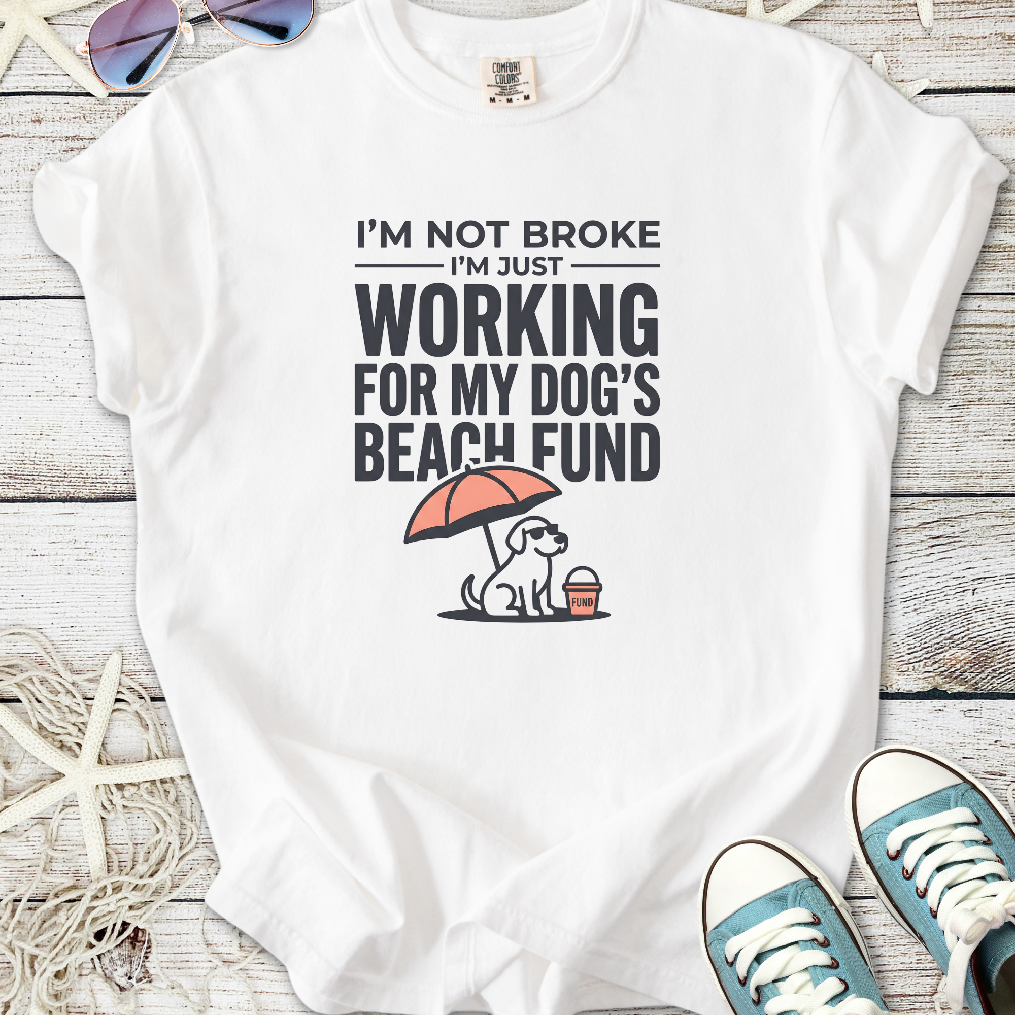 White t-shirt with humorous dog-themed graphic saying 'Working for my dog's beach fund' and an illustrated dog.