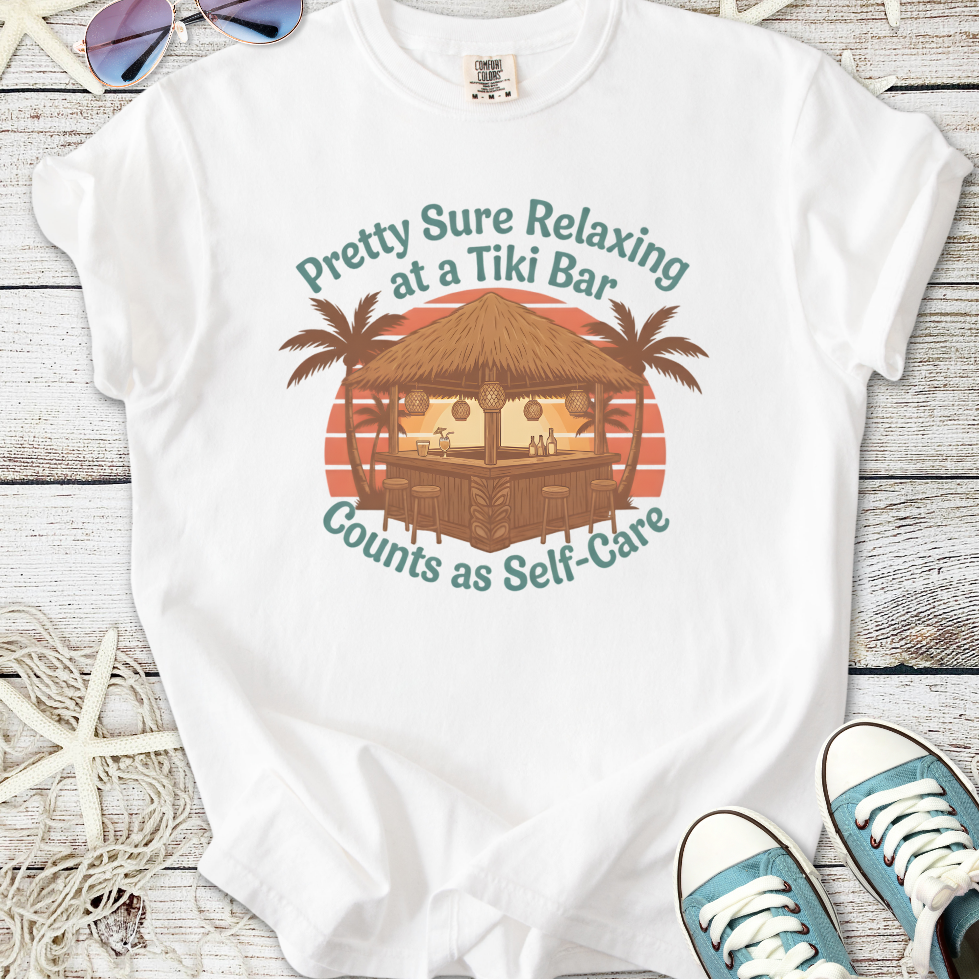 White t-shirt featuring a Tiki bar graphic with palm trees, promoting relaxation and self-care.