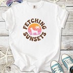 White t-shirt featuring 'Fetching Sunsets' graphic with dog silhouette and palm trees, perfect for summer.