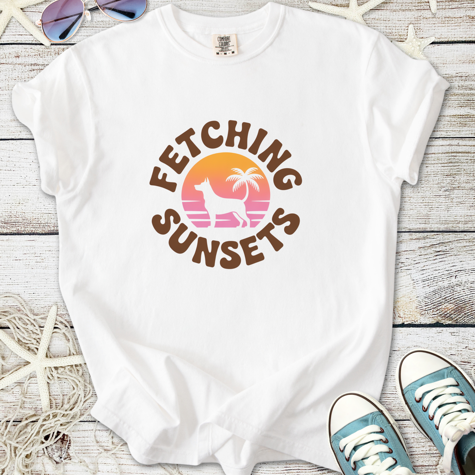 White t-shirt featuring 'Fetching Sunsets' graphic with dog silhouette and palm trees, perfect for summer.