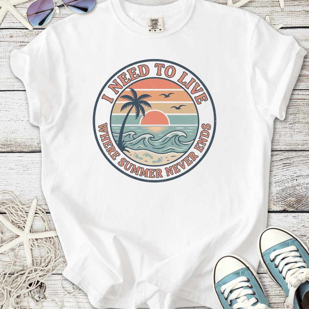 White t-shirt with 'I Need to Live' graphic featuring sunset, palm tree, and ocean waves design.