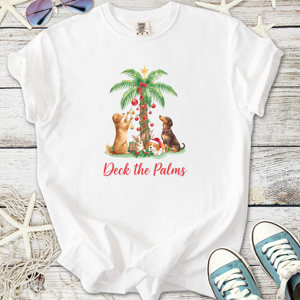 White t-shirt featuring dogs decorating a palm tree, with 'Deck the Palms' text, perfect for holiday wear.
