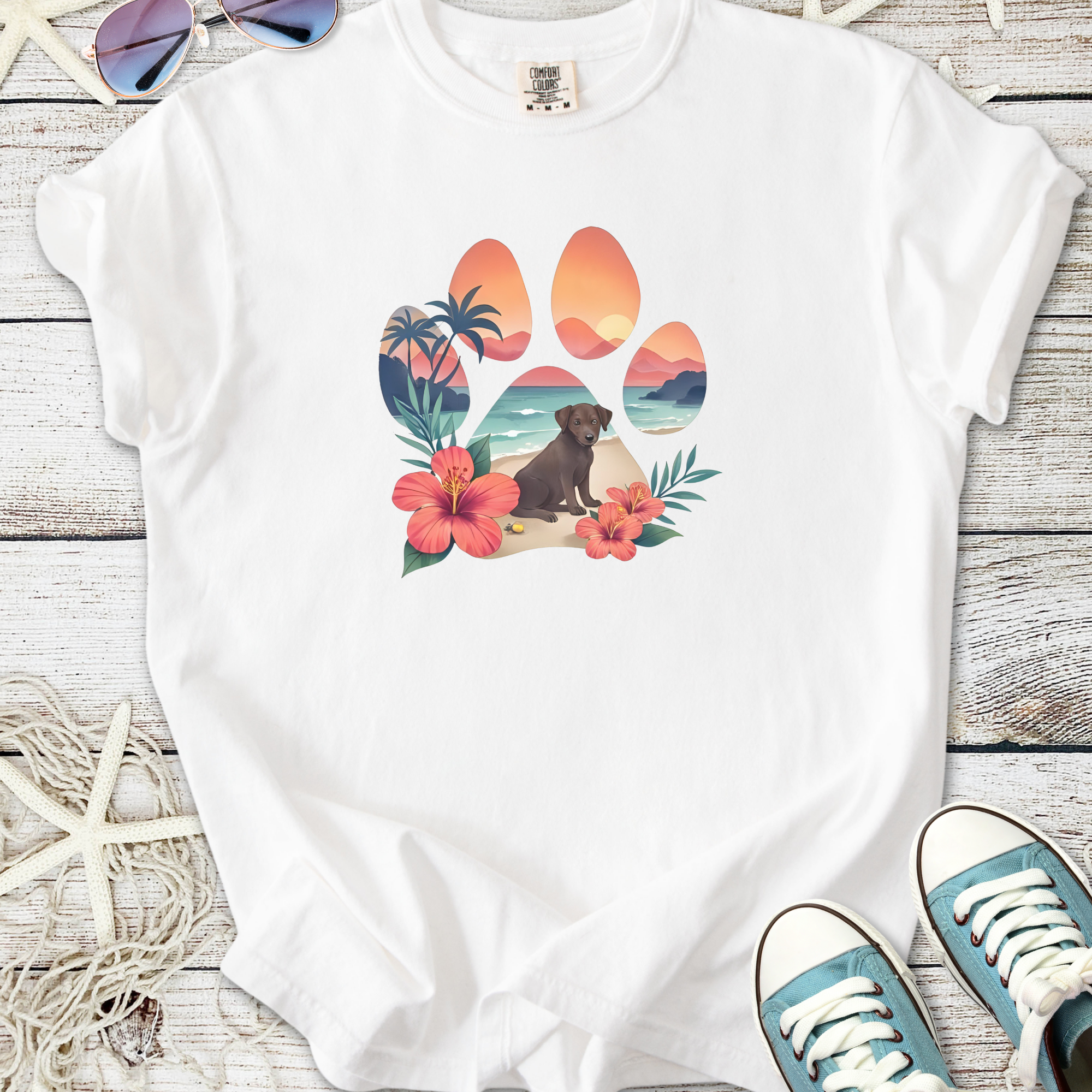 White t-shirt featuring a colorful paw print design with tropical elements and a lounging dog.