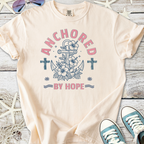 Light pink t-shirt featuring an anchor, flowers, and the phrase 'Anchored by Hope' in a casual style.
