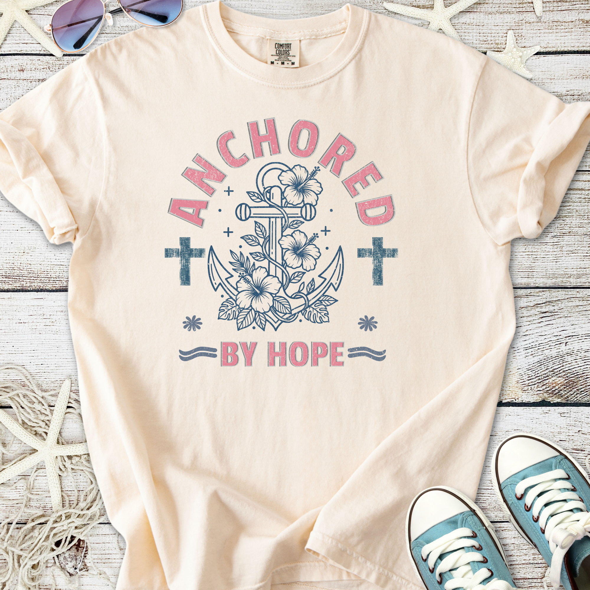 Light pink t-shirt featuring an anchor, flowers, and the phrase 'Anchored by Hope' in a casual style.