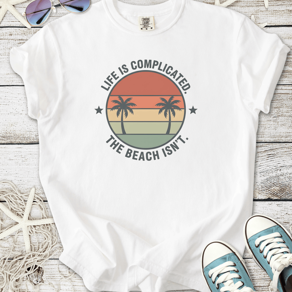 White t-shirt with palm tree graphic and 'Life is Complicated. The Beach Isn’t.' slogan.
