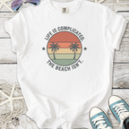 White t-shirt with palm tree graphic and 'Life is Complicated. The Beach Isn’t.' slogan.