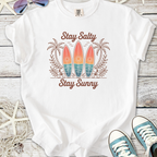 White t-shirt with 'Stay Salty Stay Sunny' graphic, featuring surfboards and palm trees design.
