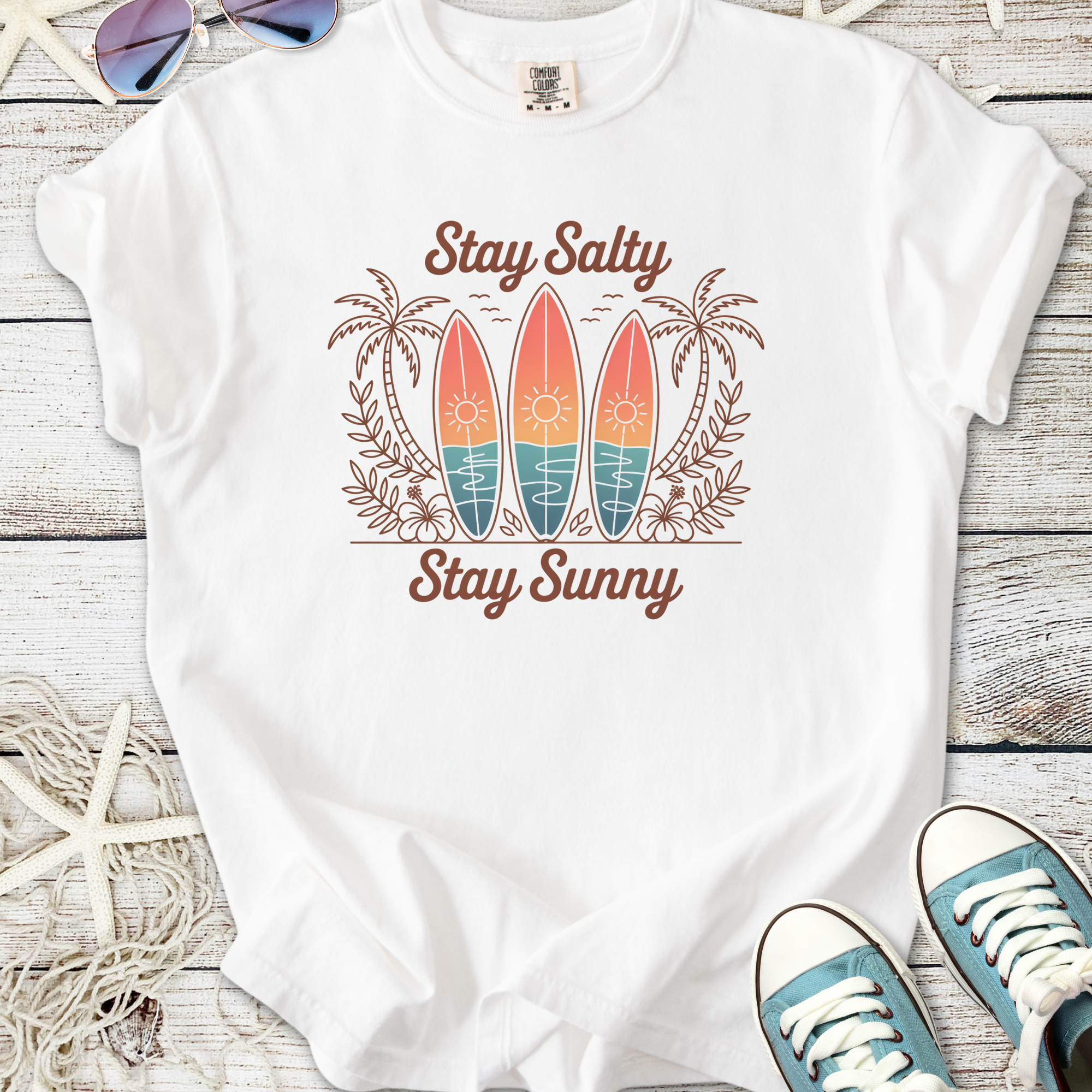 White t-shirt with 'Stay Salty Stay Sunny' graphic, featuring surfboards and palm trees design.