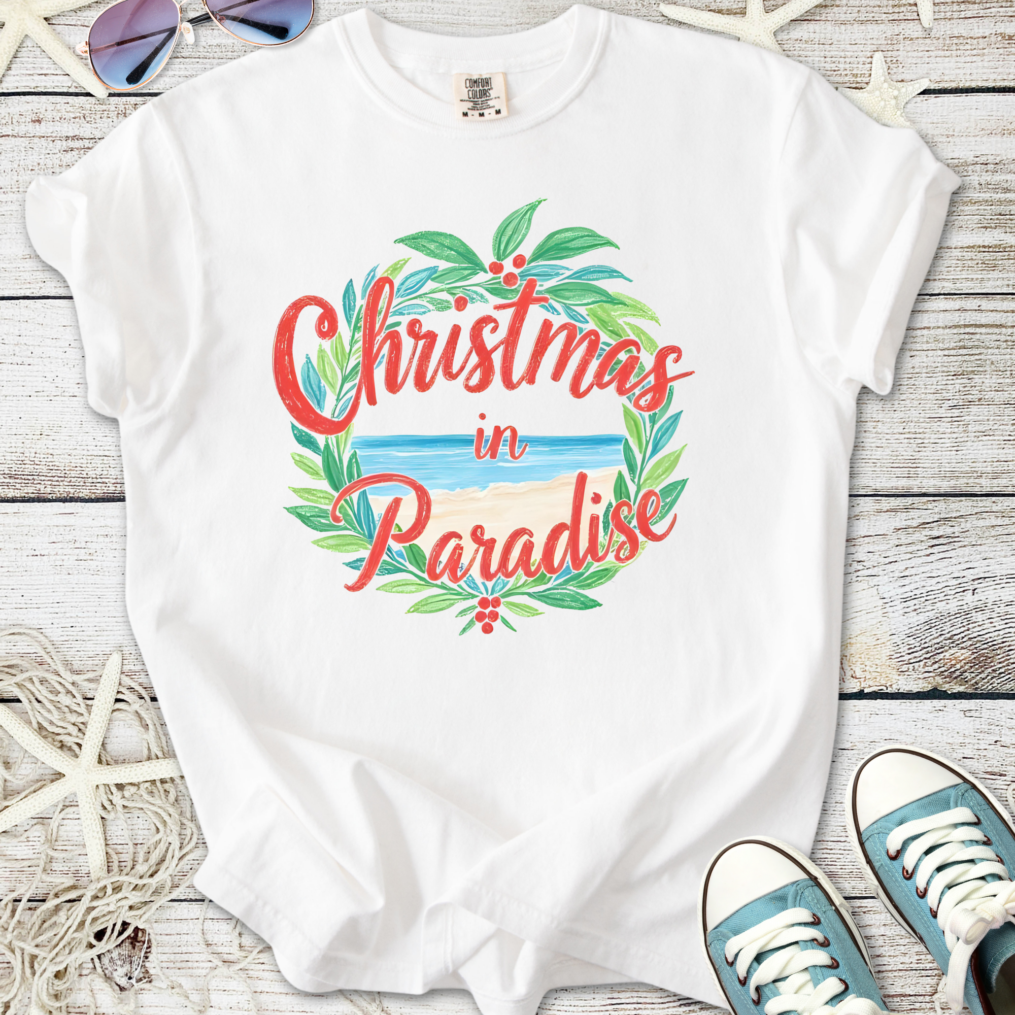 White t-shirt with 'Christmas in Paradise' graphic, featuring tropical leaves and beach design.