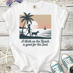 White t-shirt with beach-themed graphic, featuring a woman walking a dog and sunset design.