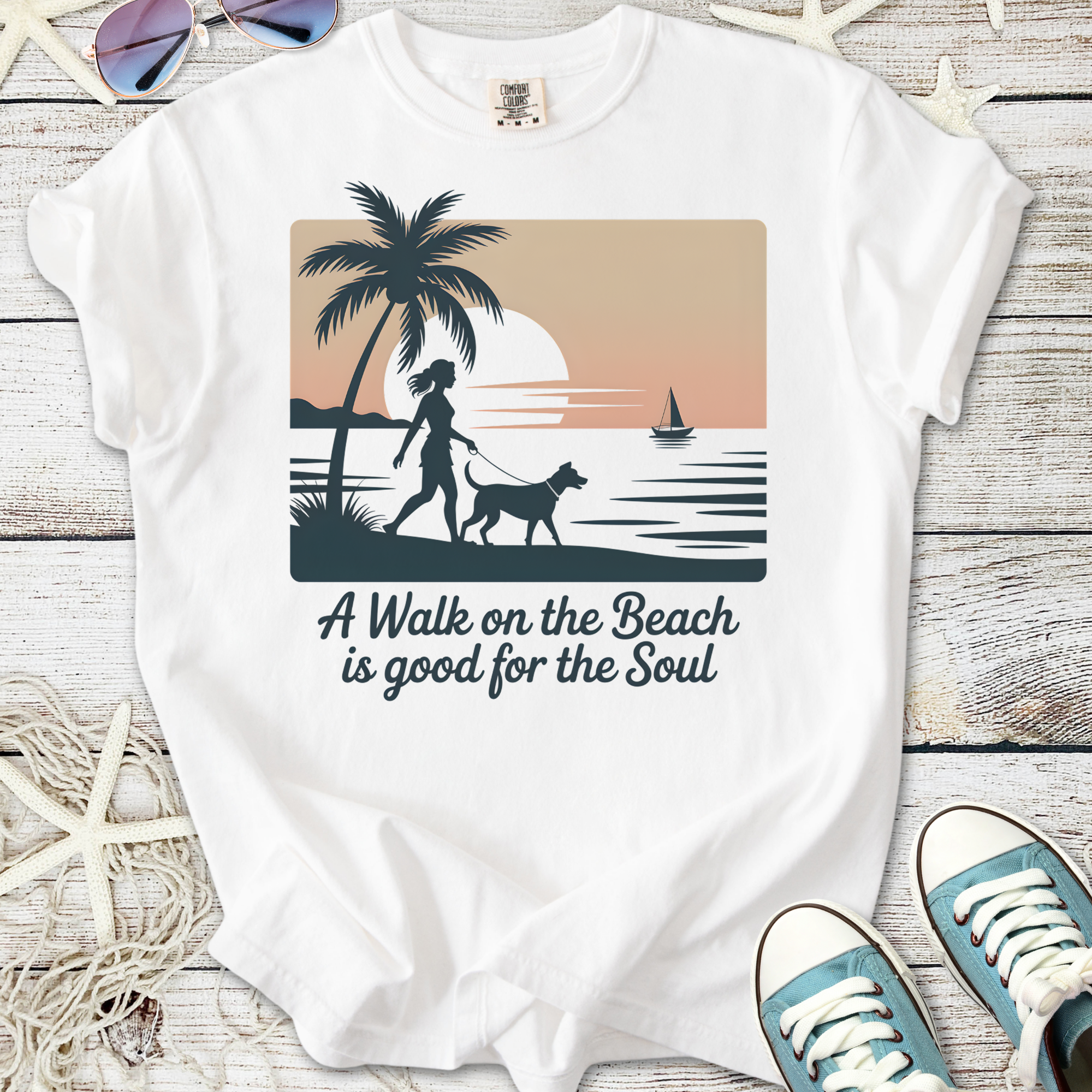 White t-shirt with beach-themed graphic, featuring a woman walking a dog and sunset design.