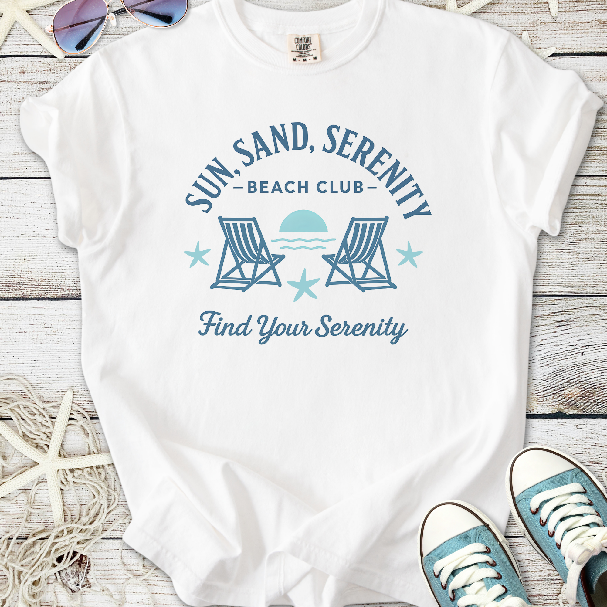 White graphic tee featuring 'Sun, Sand, Serenity Beach Club' design with beach chairs and stars.