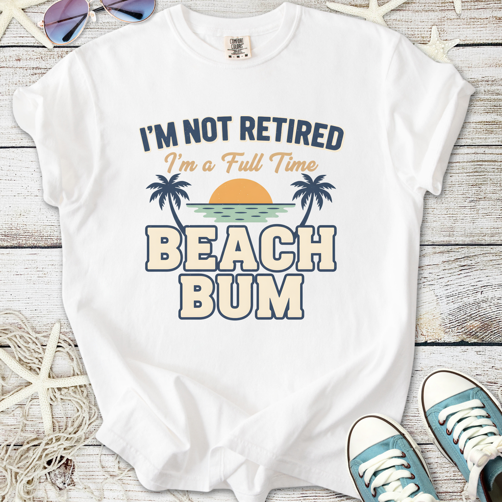 White graphic t-shirt with 'I'm Not Retired, I'm a Full Time Beach Bum' print, ideal for beach lovers.