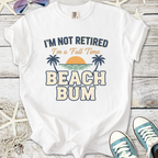 White graphic t-shirt with 'I'm Not Retired, I'm a Full Time Beach Bum' print, ideal for beach lovers.