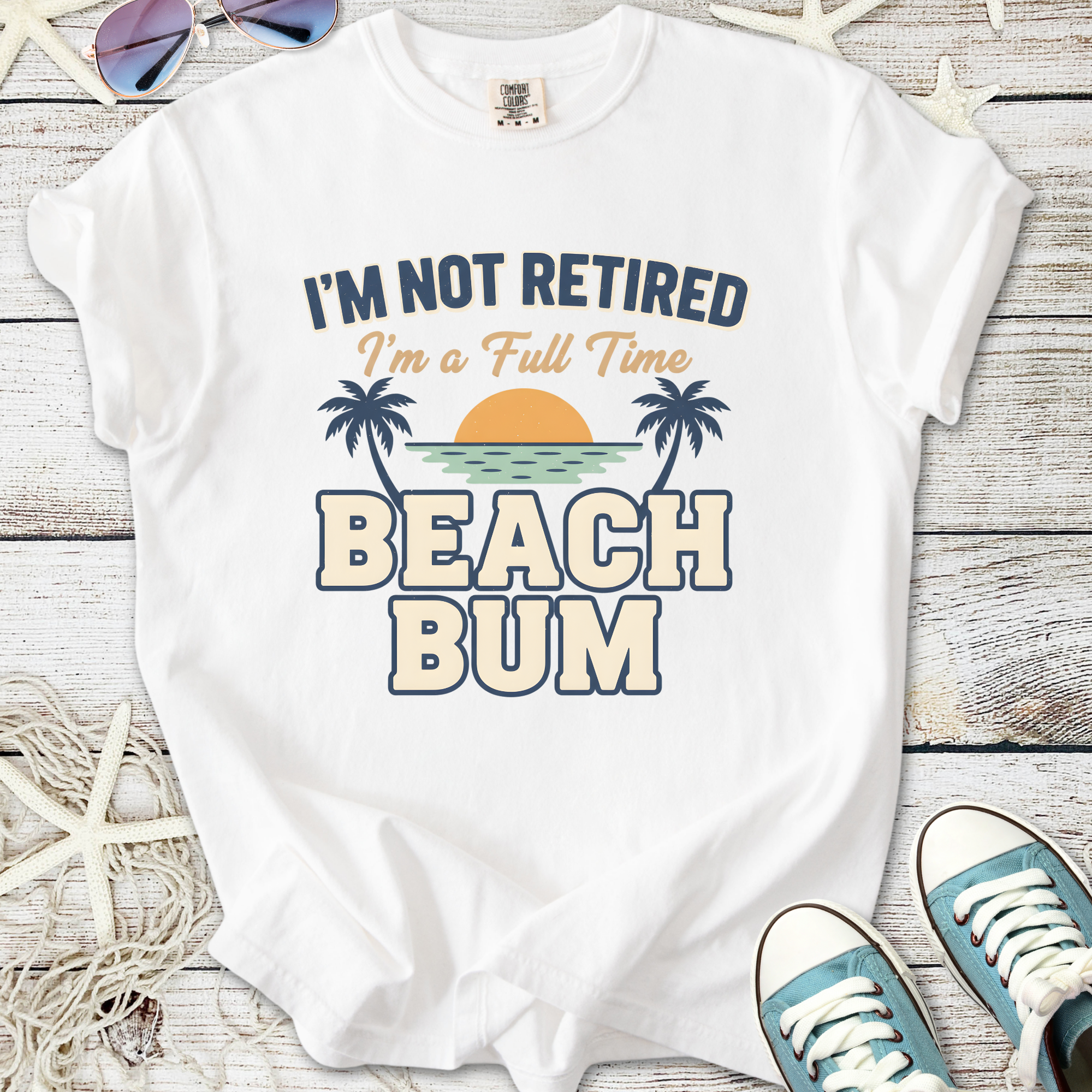 White graphic t-shirt with 'I'm Not Retired, I'm a Full Time Beach Bum' print, ideal for beach lovers.