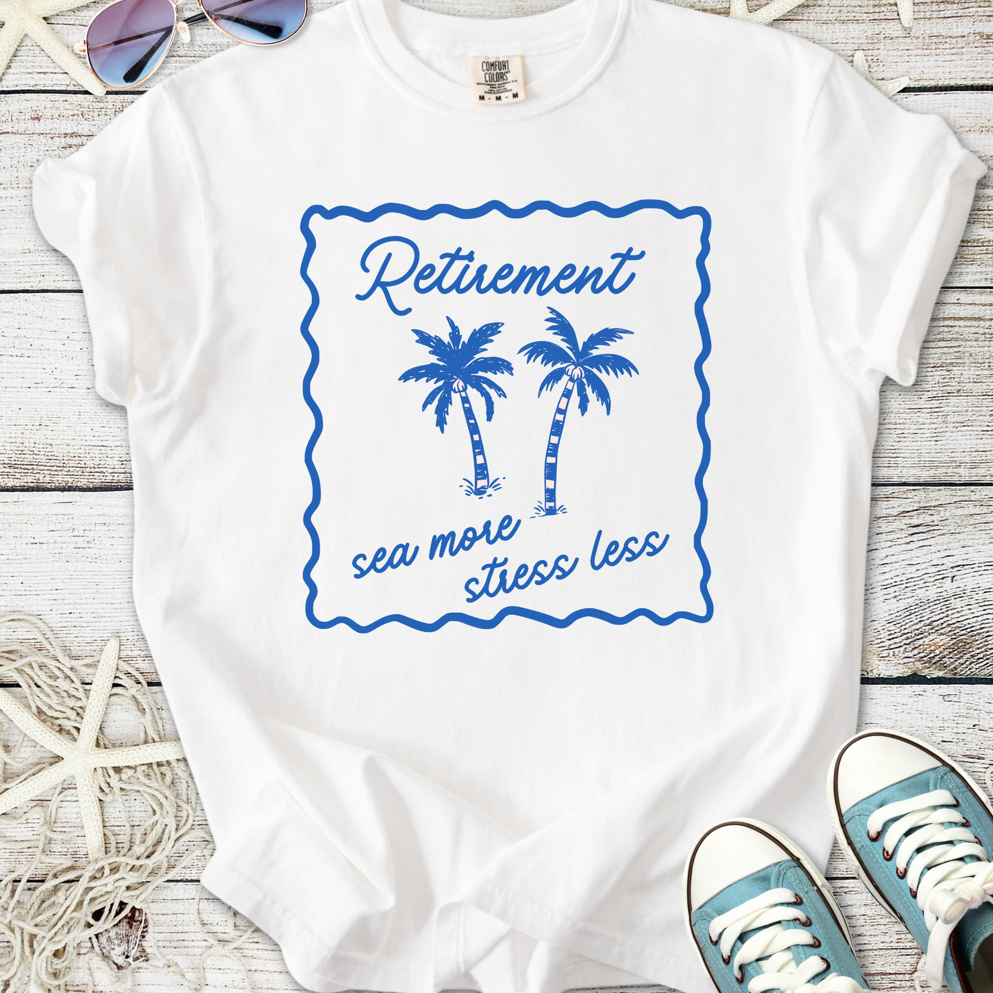 White cotton t-shirt with blue palm tree graphic and 'Retirement sea more stress less' slogan.