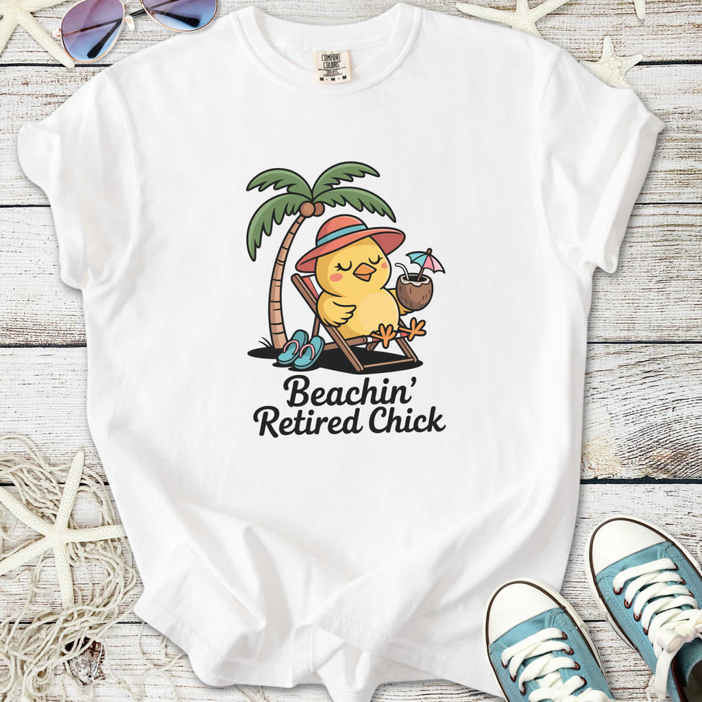 White t-shirt featuring a cartoon chick relaxing under a palm tree with drink, text 'Beachin' Retired Chick'.
