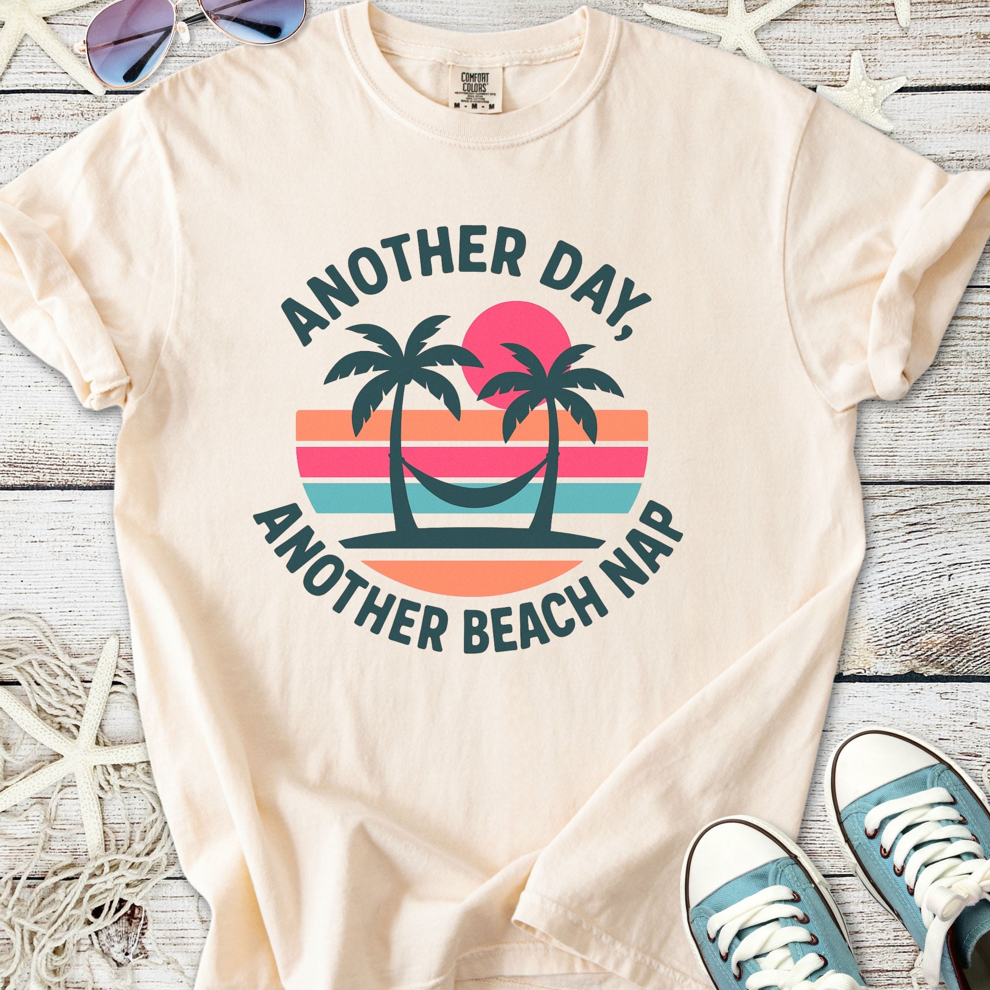 Beige graphic tee featuring palm trees and sunset design with 'Another Day, Another Beach Nap' text.