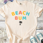 Light beige t-shirt with 'BEACH BUM' print and palm tree graphic, perfect for summer casual wear.
