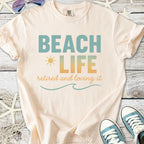 Cream beach-themed t-shirt with 'Beach Life' graphic, perfect for retirees who love the ocean.