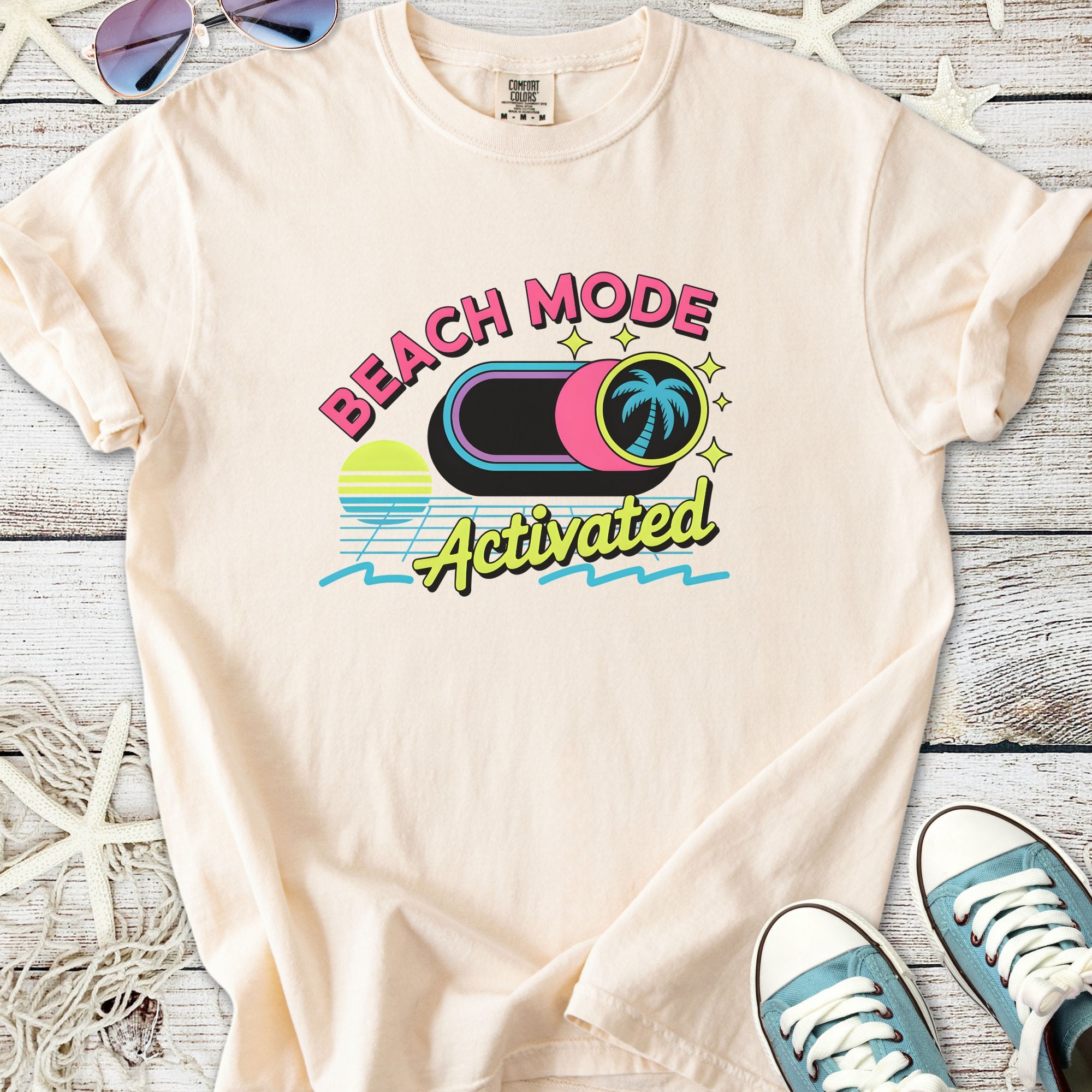 Light pink t-shirt featuring 'Beach Mode Activated' graphic with palm trees and sun, perfect for summer casual wear.